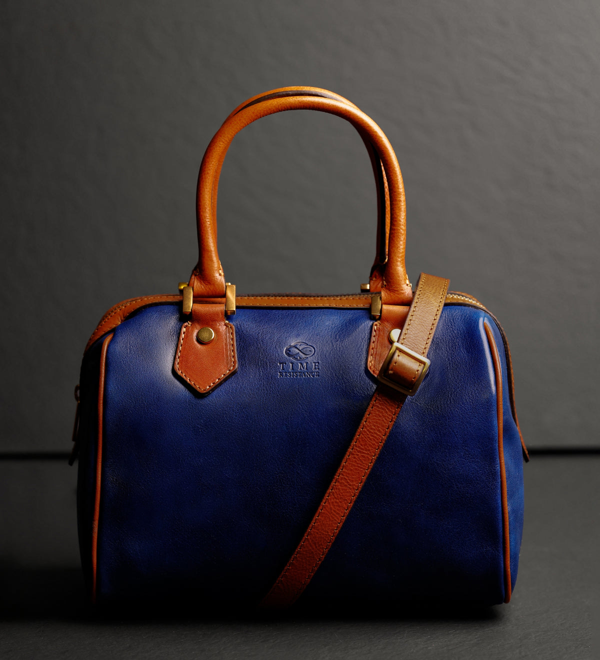 Bauletto Little Dorrit blu su sfondo scuro con la tracolla appoggiata sul davanti
