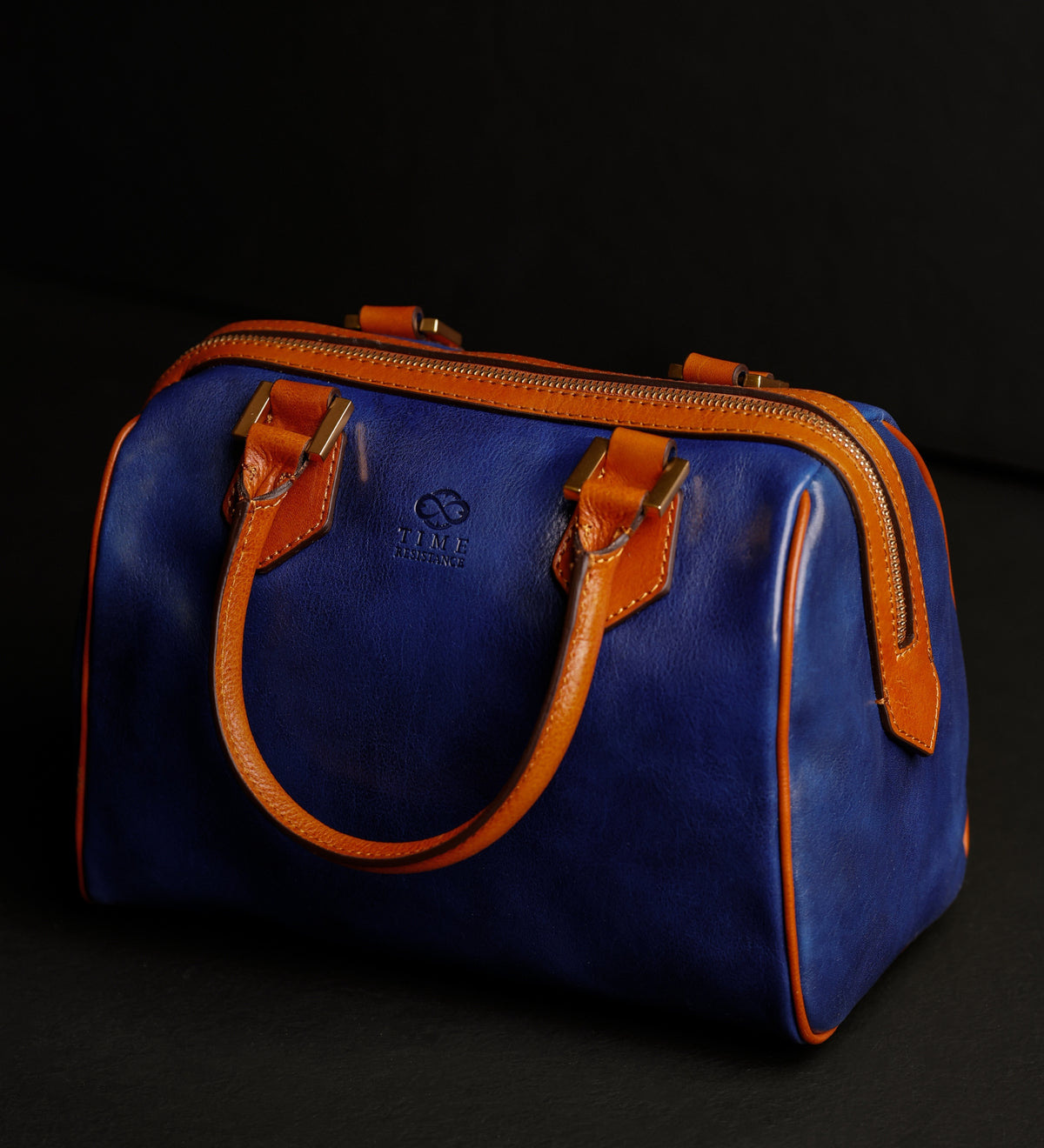 Bauletto Little Dorrit blu su sfondo scuro, inclinato per mostrare la cinghia con fibbia color cuoio