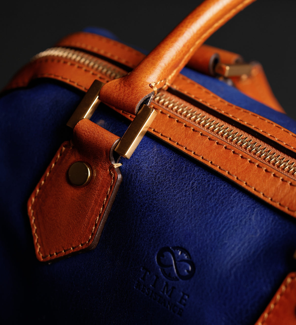 Dettaglio ravvicinato della linguetta in pelle color cuoio e del bottone in ottone sul bauletto Little Dorrit blu