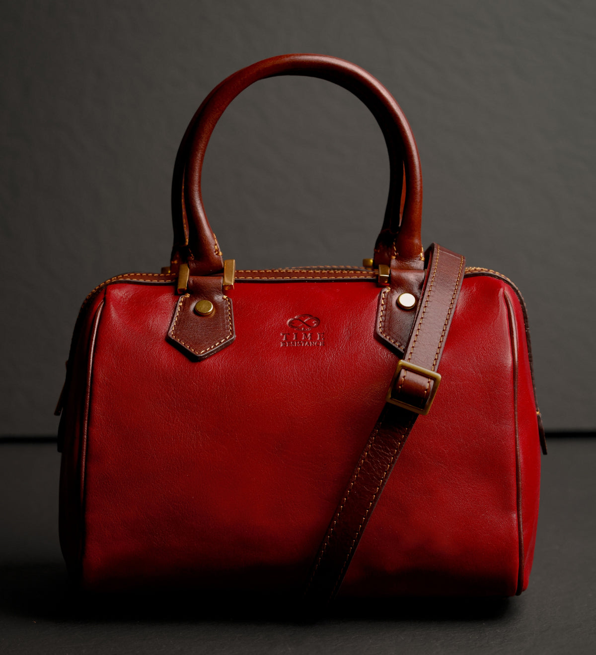 Bauletto Little Dorrit rosso su sfondo scuro con la tracolla appoggiata sopra