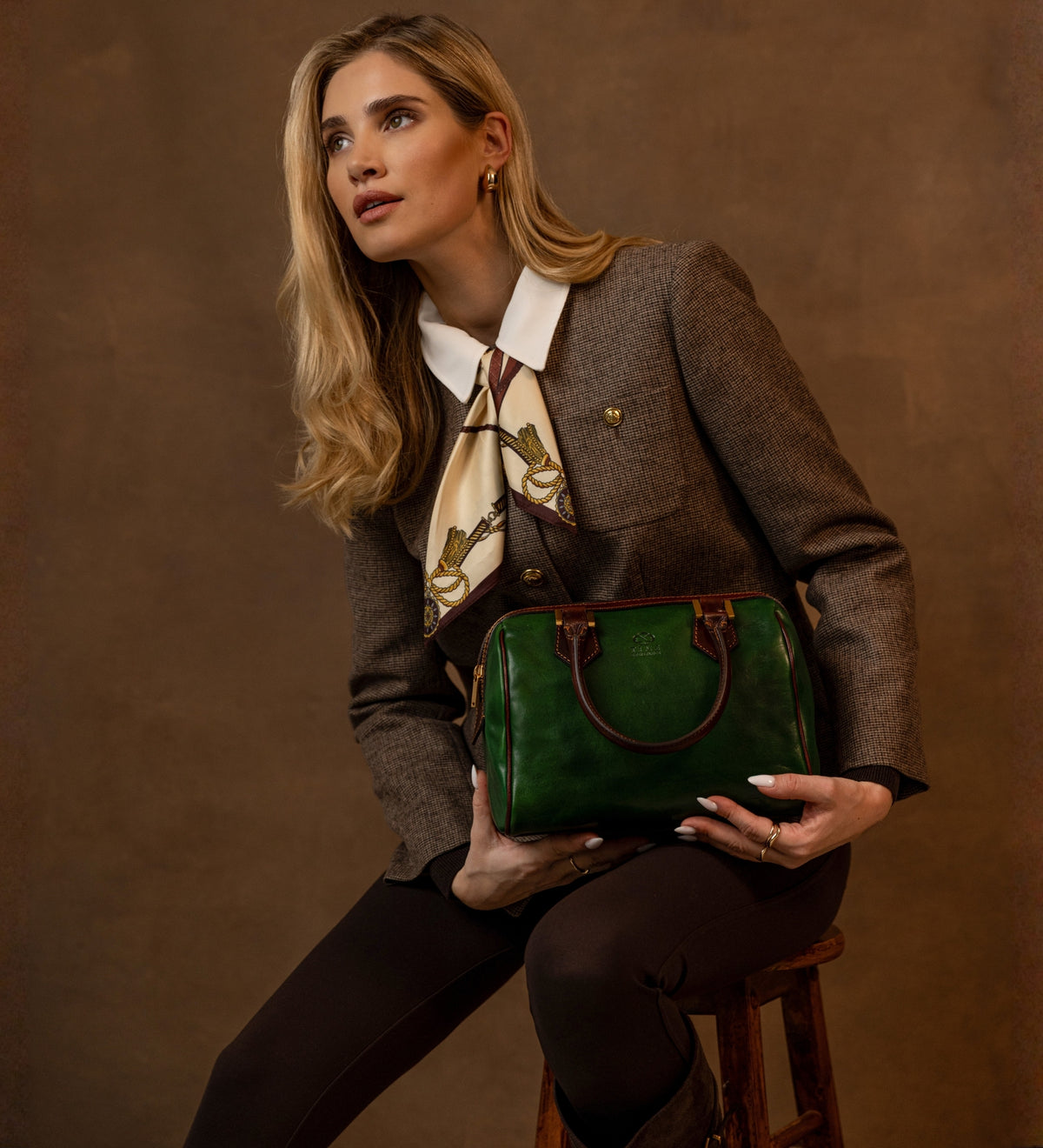 Donna con blazer in tweed che tiene il bauletto Little Dorrit verde sulle ginocchia