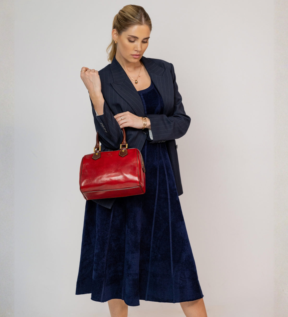 Donna con blazer gessato che tiene il bauletto Little Dorrit rosso per il manico